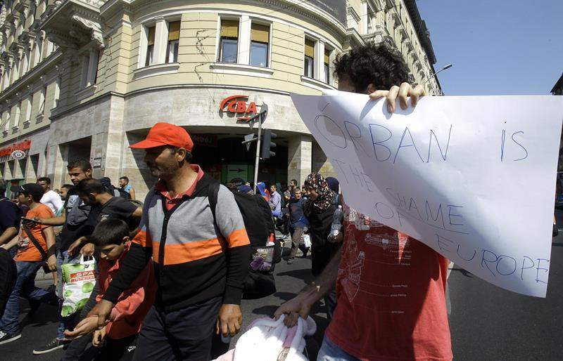 A migrant holds a paper with a text, ‘Orban (Hugarian Prime Minister) the shame of Europe’, as migrants walking in Budapest downtown after leaving the transit zone of the Budapest main train station.