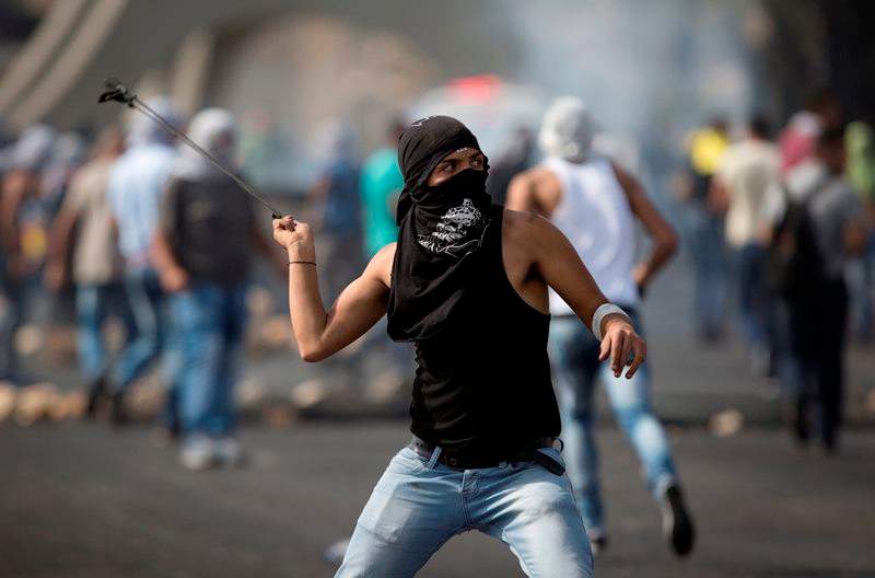 A Palestinian hurls a stone during clashes with Israeli troops near Ramallah, West Bank, Monday, Oct. 12, 2015.