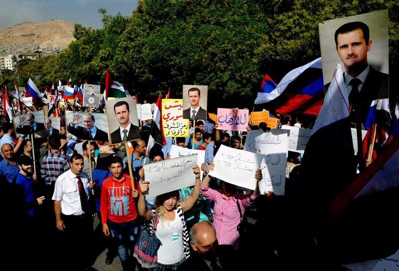 This photo released by the Syrian official news agency SANA shows, Syrians holding photos of Syrian President Bashar Assad and Russian Prime Minister Vladimir Putin, during a protest to thank Moscow for its intervention in Syria, in front of the Russian embassy in Damascus, Syria, Tuesday, Oct. 13, 2015.