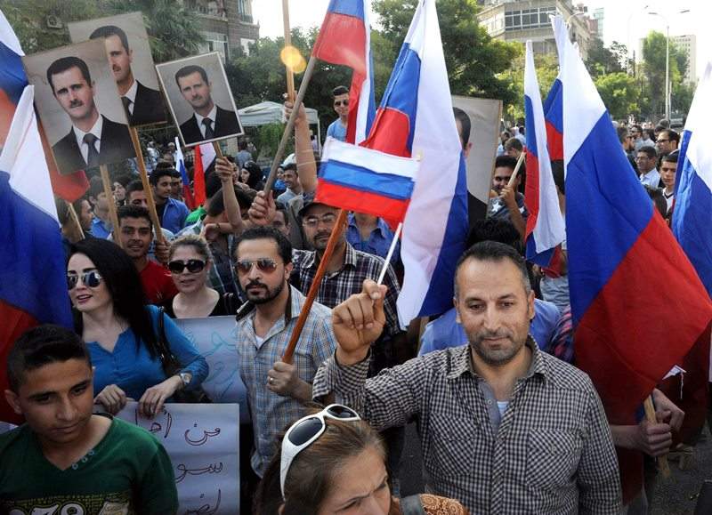 This photo released by the Syrian official news agency SANA, shows Syrians holding photos of Syrian President Bashar Assad and Russian flags, during a protest to thank Moscow for its intervention in Syria, in front of the Russian embassy in Damascus, Syria, Tuesday, Oct. 13, 2015.