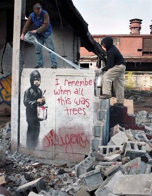 This May 11, 2010 file photo shows the founders of the art gallery 555 Arts, Carl W. Goines, left, and Monte Martinez, wrapping artwork by popular graffiti artist Banksy at the abandoned Packard car plant in Detroit. 