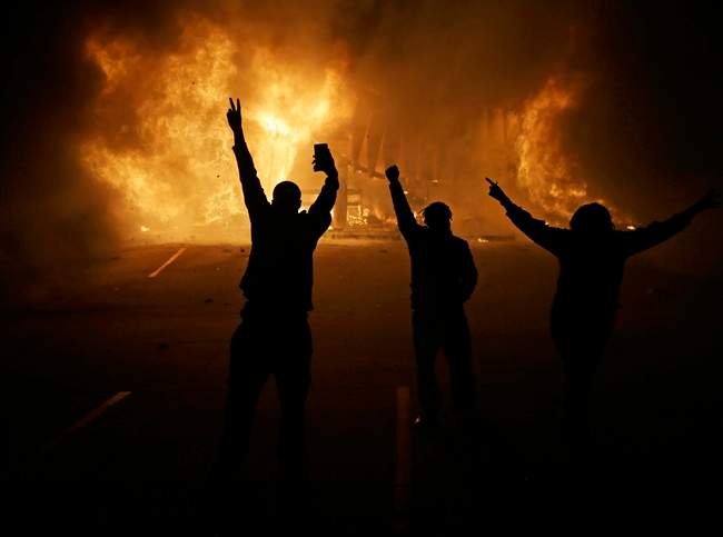 In this Nov. 25, 2014, file photo, people watch as stores burn in Ferguson, Mo., after a grand jury decided not to indict Ferguson police Officer Darren Wilson in the death of Michael Brown, the unarmed, black 18-year-old whose fatal shooting sparked sometimes violent protests. 