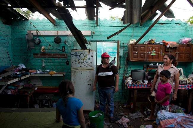Josefina Magana Ruiz, center, surveys her home damaged by Hurricane Patricia, in La Fortuna, Mexico, Saturday, Oct. 24, 2015. Hurricane winds tore off much of the roof of the two-room home where seven people live, soaking mattresses and destroying belongings.