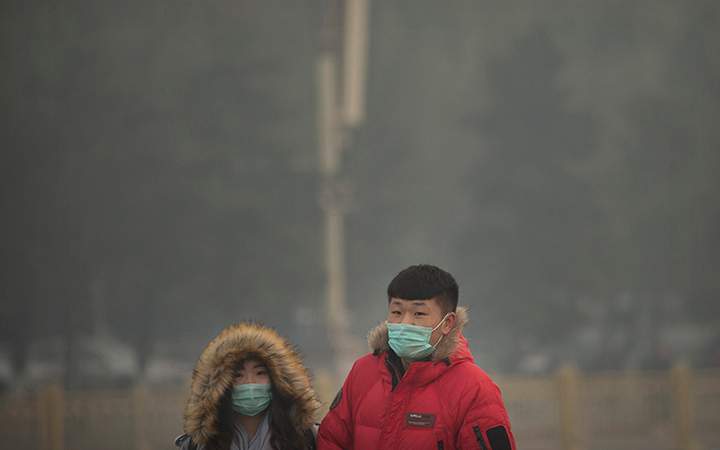 People wearing face masks walk across Tiananmen Square on a day with poor air quality in Beijing, Saturday, Nov. 28, 2015.