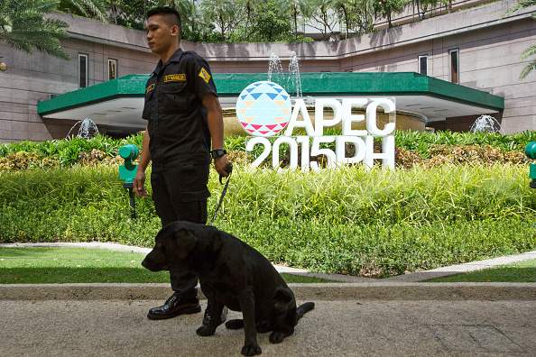 A security dog handler stands as signage for the Asia-Pacific Economic Cooperation (APEC) CEO Summit is displayed outside the Makati Shangri-La Hotel, in the Makati district of Manila, the Philippines, on Monday, Nov. 16, 2015. 