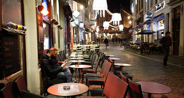 A man smokes a cigarette and looks at his smartphone under a heating lamp, in what would normally be a busy tourist area of central Brussels, Monday, Nov. 23, 2015.