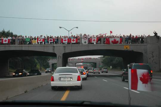 People wave flags along the Highway of Heroes as Jordan Anderson’s casket drives by.