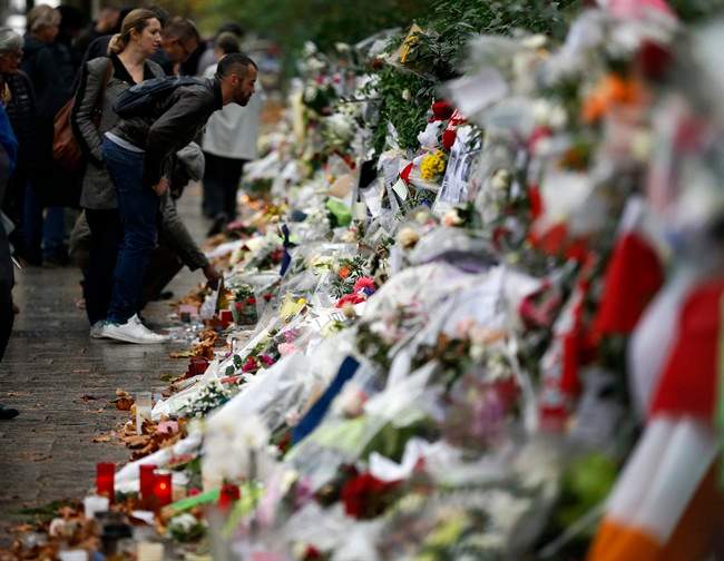 People look at flowers and card tributes placed outside the Bataclan concert hall in Paris, Thursday, Nov. 19, 2015.