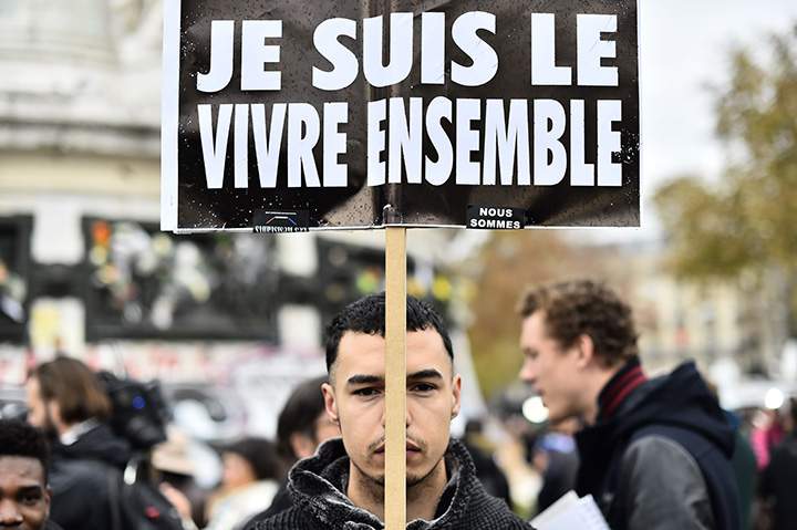 A man holds a placard reading “I am the living together” as people gather after observing a minute of silence to pay tribute to victims of the attacks in Paris.