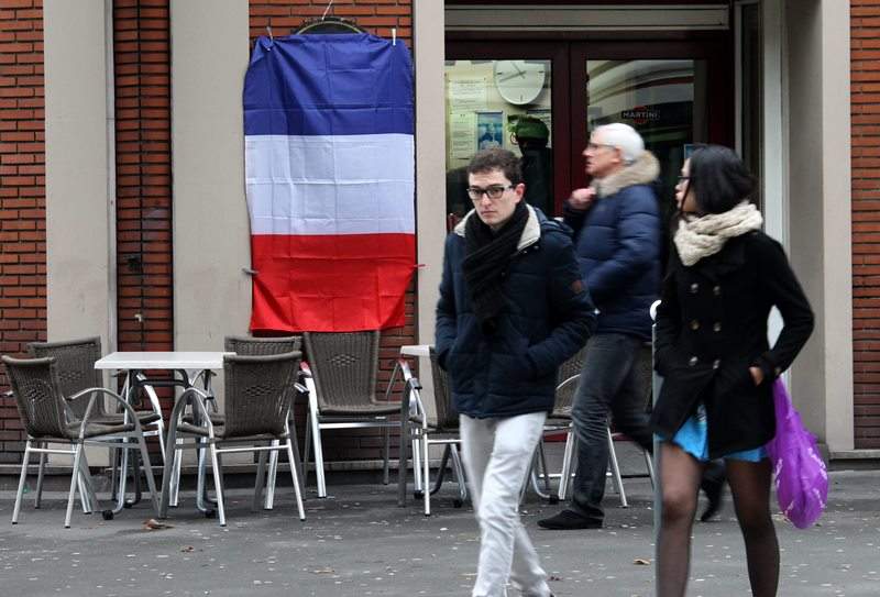 People walk in front of a French flags hanging from a empty terrace in Lille, northern France, Friday, Nov. 27, 2015..