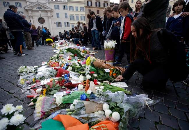 People gather in front of flowers that were laid outside the French embassy in Rome, Saturday, Nov. 14, 2015. French police on Saturday hunted possible accomplices of eight assailants who terrorized Paris concert-goers, cafe diners and soccer fans with a coordinated string of suicide bombings and shootings in France's deadliest peacetime attacks. (AP Photo/Gregorio Borgia).