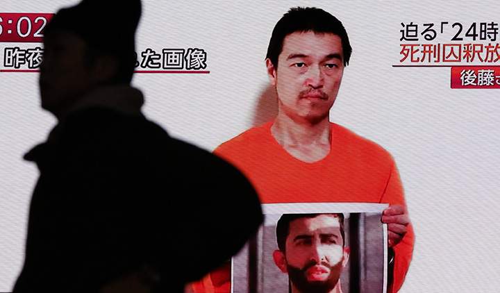 In this Jan. 28, 2015 photo, a man walks by a screen showing TV news reports of a YouTube posted by a militant group on Jan. 27, purportedly showing a still photo of Japanese hostage Kenji Goto holding what appears to be a photo of Jordanian pilot Lt. Muath al-Kaseasbeh, in Tokyo.