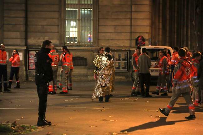 People wearing survival blanket stand near Rue de Charonne, one of the sites targetted in Friday's shootings, in Paris, Saturday, Nov. 14, 2015.