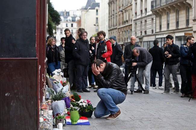 A man holds his head in his hands as he lays flowers in front of the Carillon cafe, in Paris, Saturday, Nov.14, 2015. French President Francois Hollande vowed to attack Islamic State without mercy as the jihadist group admitted responsibility Saturday for orchestrating the deadliest attacks inflicted on France since World War II.