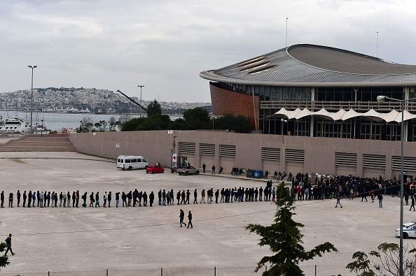 Migrants and refugees line up for food outside of a temporary housing facility for migrants located in a former Olympic hall in Faliro suburb of Athens on December 11, 2015. 