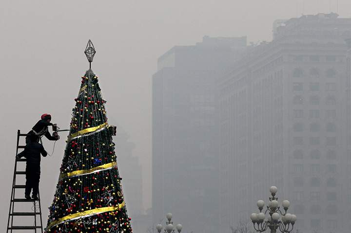 Workers install a Christmas tree on display outside a shopping mall during a day of heavy pollution in Beijing, Tuesday, Dec. 8, 2015.