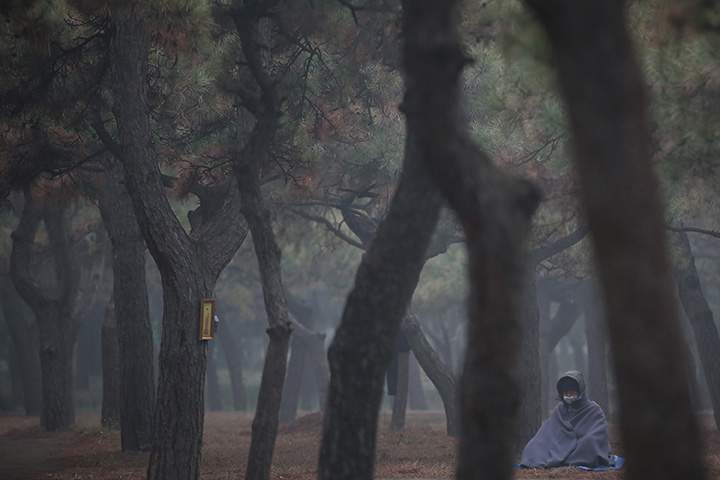 A Buddhist wearing mask meditates at Temple of Heaven Park during a day of heavy pollution on December 9, 2015 in Beijing, China.