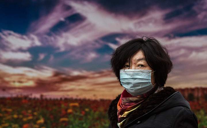 A woman wears a mask to protect against pollution as she passes a picture of a sunset advertising tourism to China’s Hebei province on December 8, 2015 in Beijing.
