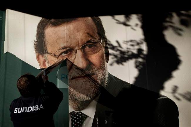 A worker removes a campaign poster for the national elections depicting Spain's acting Prime Minister and Popular Party candidate Mariano Rajoy, in Madrid, Monday, Dec. 21, 2015. 