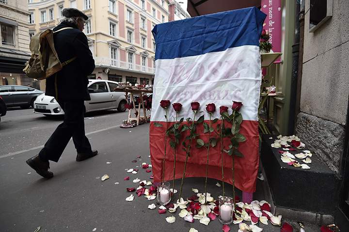 A man walks past a French national flag put outside a flower shop on November 27, 2015 in Strasbourg, eastern France, during the National Tribute to the 130 people killed in the November 13 Paris attacks.  
