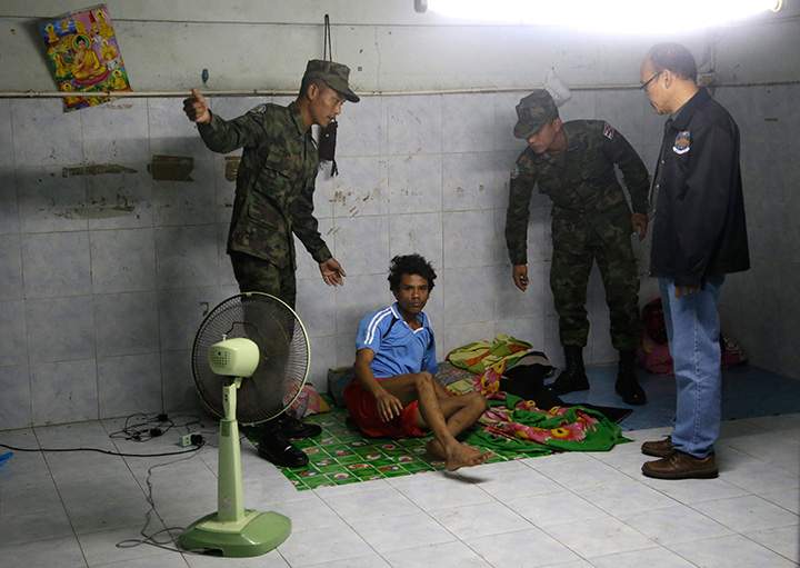 In this Monday, Nov. 9, 2015 photo, Thai soldiers and a member of the Department of Special Investigation wake up a worker during a raid on a shrimp shed in Samut Sakhon, Thailand.