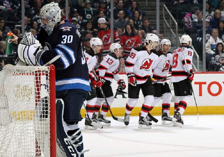 Winnipeg Jets goalie Connor Hellebuyck turns away as the New Jersey Devils celebrate a first period goal.