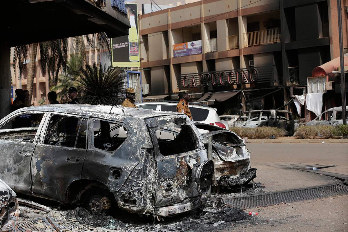 Soldiers walk past burnt cars outside the Cappuccino cafe that was attacked Saturday by suspected militants in Ouagadougou, Burkina Faso, Sunday, Jan. 17, 2016.