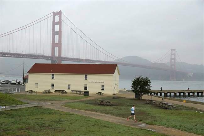 In this photo taken Tuesday, Dec. 8, 2015, a jogger goes past the Warming Hut Cafe with the Golden Gate Bridge in the background in San Francisco.