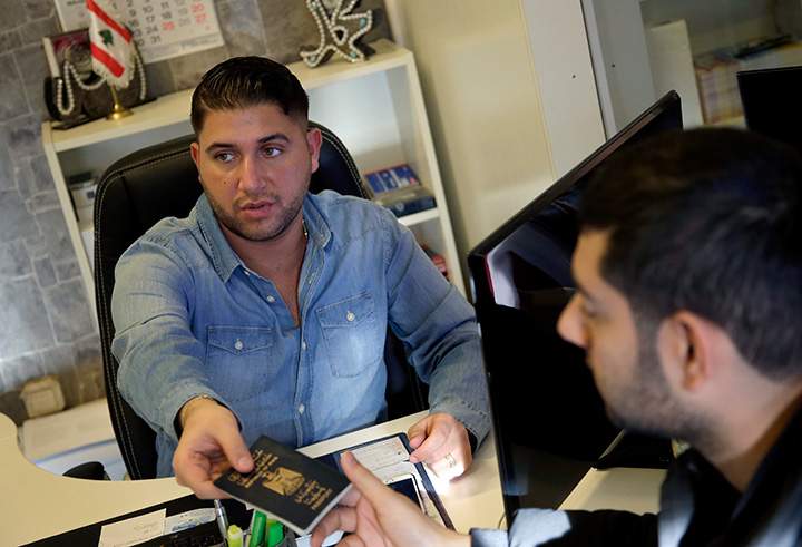 In this Jan. 26, 2016 photo travel agent Alaa Hadrous, left, hands over a passport to traveler Hussein Hotuman from Iraq, right, at Gulf Travels travel agency in Berlin, Germany. 