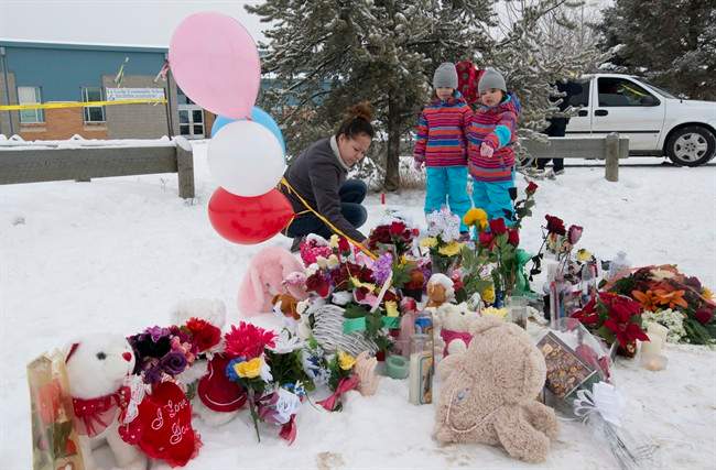 Tashina Montgrand lays flowers outside the La Loche Community School as her daughters Tayala and Tayvah look on in La Loche, Sask.