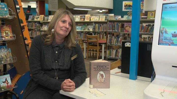 Kathleen Troppman with the St. Albert Public Library sits next to a Lucy Maud Montgomery book. The book was returned by a man 38 years after it was loaned out to his mother.