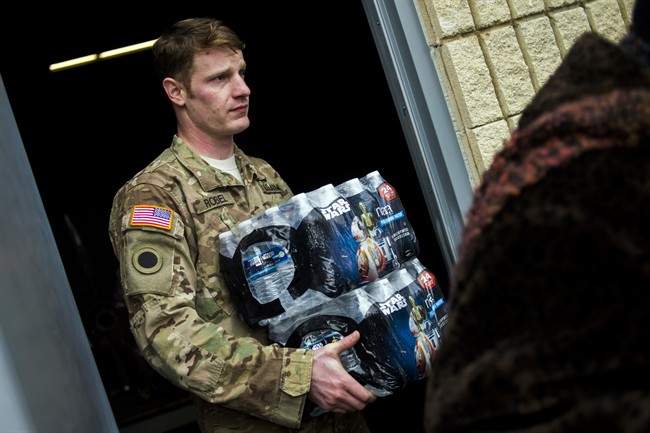 Michigan National Guard Staff Sgt. Stephen Robel helps carry a case of water to the vehicle of Flint resident Karand Houston.