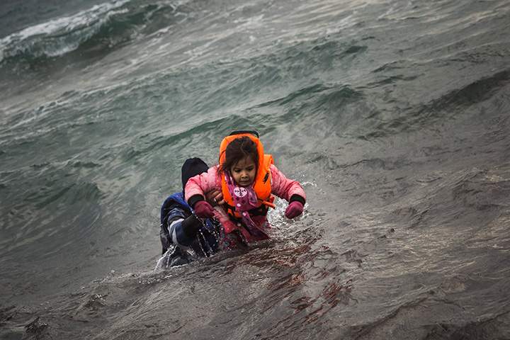 A man carries a child as they try to reach the shore after falling into the sea while disembarking from a dinghy on which they crossed a part of the Aegean Sea with other refugees and migrants, from Turkey to the Greek island of Lesbos, on Sunday, Jan. 3, 2016. 