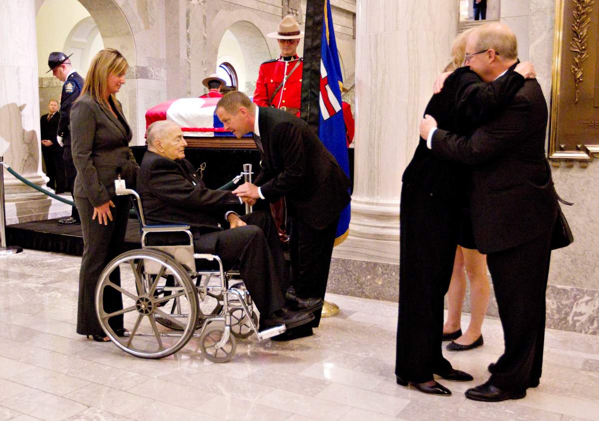 Former Alberta premier Don Getty (left in wheelchair), shakes hands with Joe Lougheed, Peter Lougheed’s son as his wife Margaret Getty, right, hugs Stephen Lougheed, another son, as they pay their respects to former Alberta premier Peter Lougheed as his body lies in state at the Alberta Legislature on Monday September 17, 2012. in Edmonton, Alberta. THE CANADIAN PRESS/Jason Franson