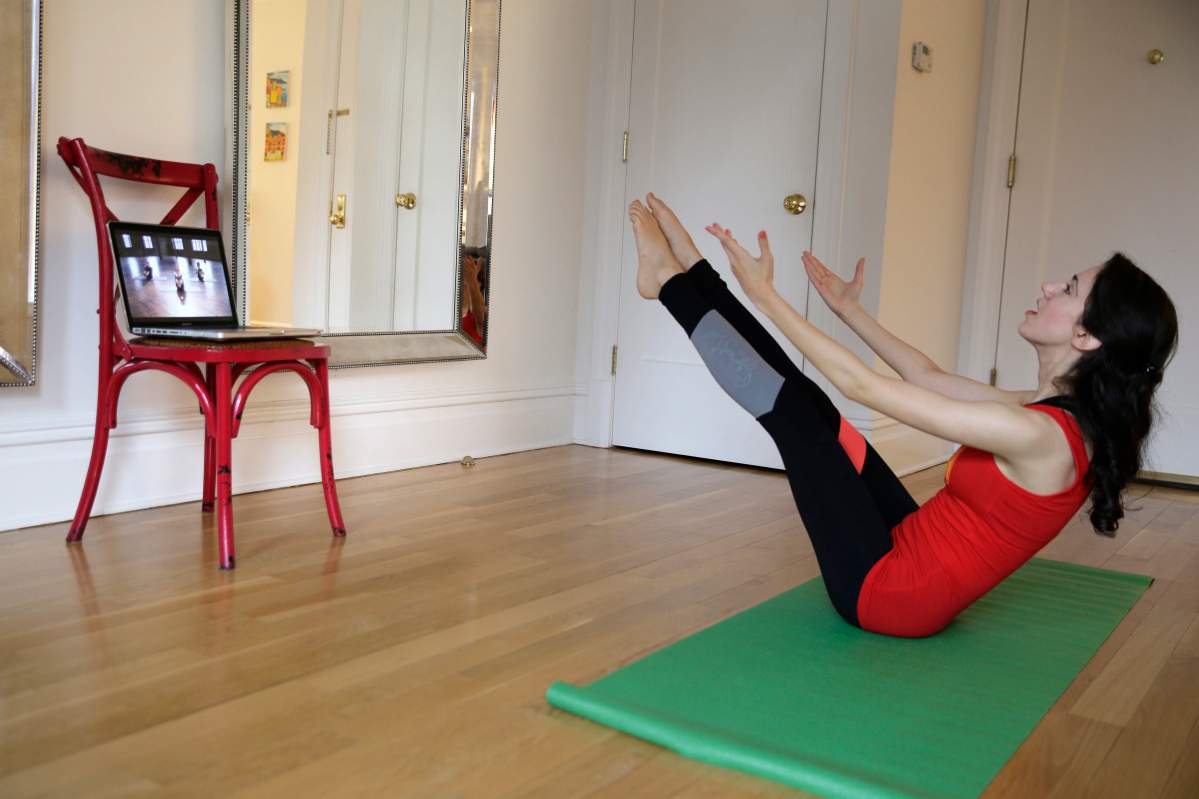 In this April 14, 2015 photo, Christina Macchiarola demonstrates how she uses the Crunch Live fitness app to work out in her apartment in New York. Crunch Live includes many of the workouts that earned the brand a devoted following and have been retired from their brick and mortar gyms.  