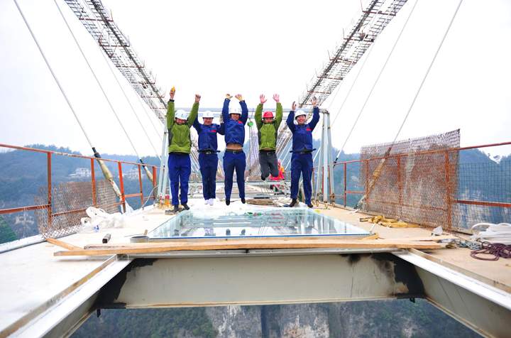 These brave souls, workers on the glass-bottomed Zhangjiajie Grand Canyon suspension bridge, jump on a glass panel, one of the first to be installed.