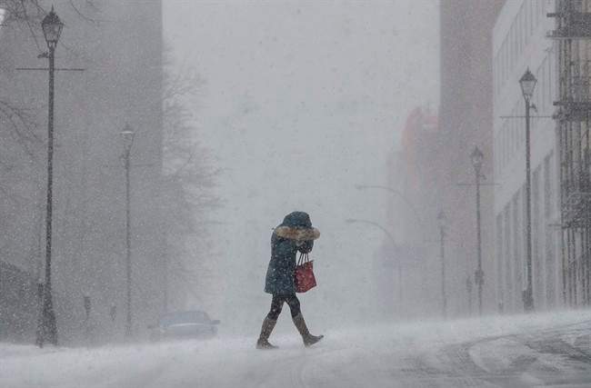 A woman shields her face from wind-swept snow during a winter storm in Halifax on Monday, Feb. 8, 2016.