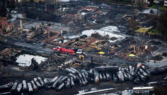 FILE - In this July 9, 2013 file photo, workers comb through debris after a train derailed causing explosions of railway cars carrying crude oil in Lac-Megantic, Quebec. A government watchdog says federal regulators are failing to refer serious safety violations involving freight rail shipments of crude oil for criminal prosecution.
