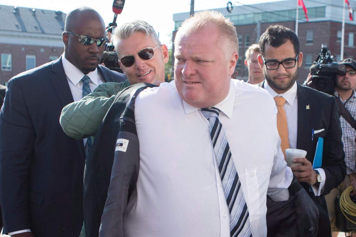 Rob Ford, right centre, is helped with his jacket by his sobriety coach Bob Marier, left centre, while his driver and personal security guard Jerry Agyemang, left, and Communications Officer Amin Massoudi look on as they arrive at an announcement at a TTC transit yard in Toronto on Friday, July 11, 2014.