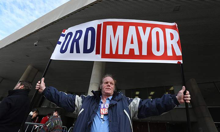 Kenny Neville holds a Rob Ford election campaign sign outside of city hall ahead of the funeral procession to St. James Cathedral in Toronto for the funeral of former mayor Rob Ford on Wednesday, March 30, 2016.