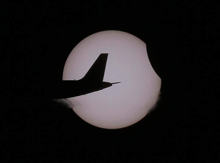 An Air Asia passenger plane flies as a partial solar eclipse occurs Wednesday, March 9, 2016 as seen from Taguig city, east of Manila, Philippines.