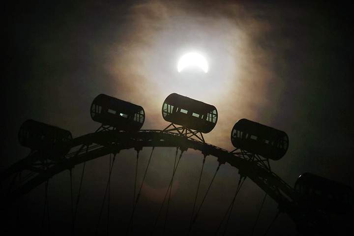 A partial solar eclipse is seen behind passenger capsules of the Singapore Flyer Wednesday, March 9, 2016, in Singapore.