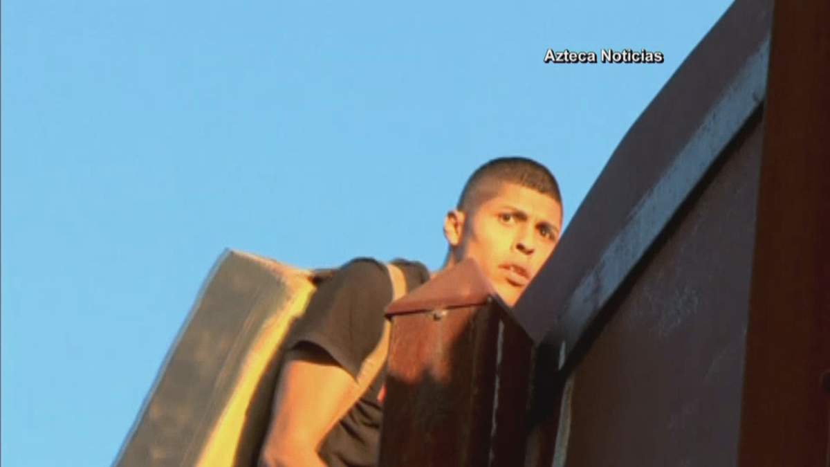 A suspected drug smuggler scaling a tall border fence from Mexico into the U.S.