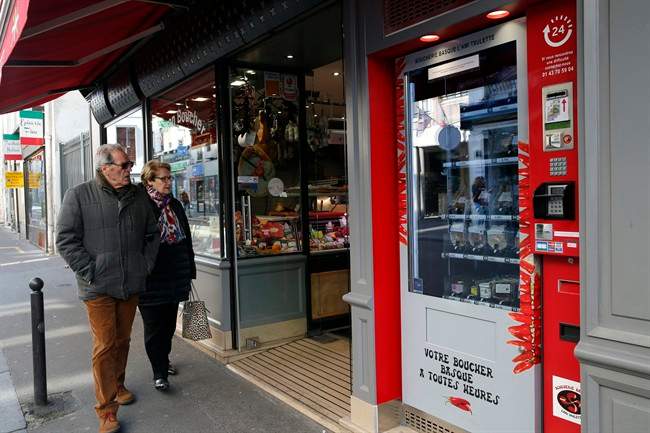 Residents watch the first meat vending machine installed in the French capital, in Paris, Tuesday, March 15, 2016. With their beloved baguette already available 24 hours a day, it seems only logical that Parisians can now get the Bayonne ham and Basque pate that goes so well with it from the first meat vending machine installed in the French capital.