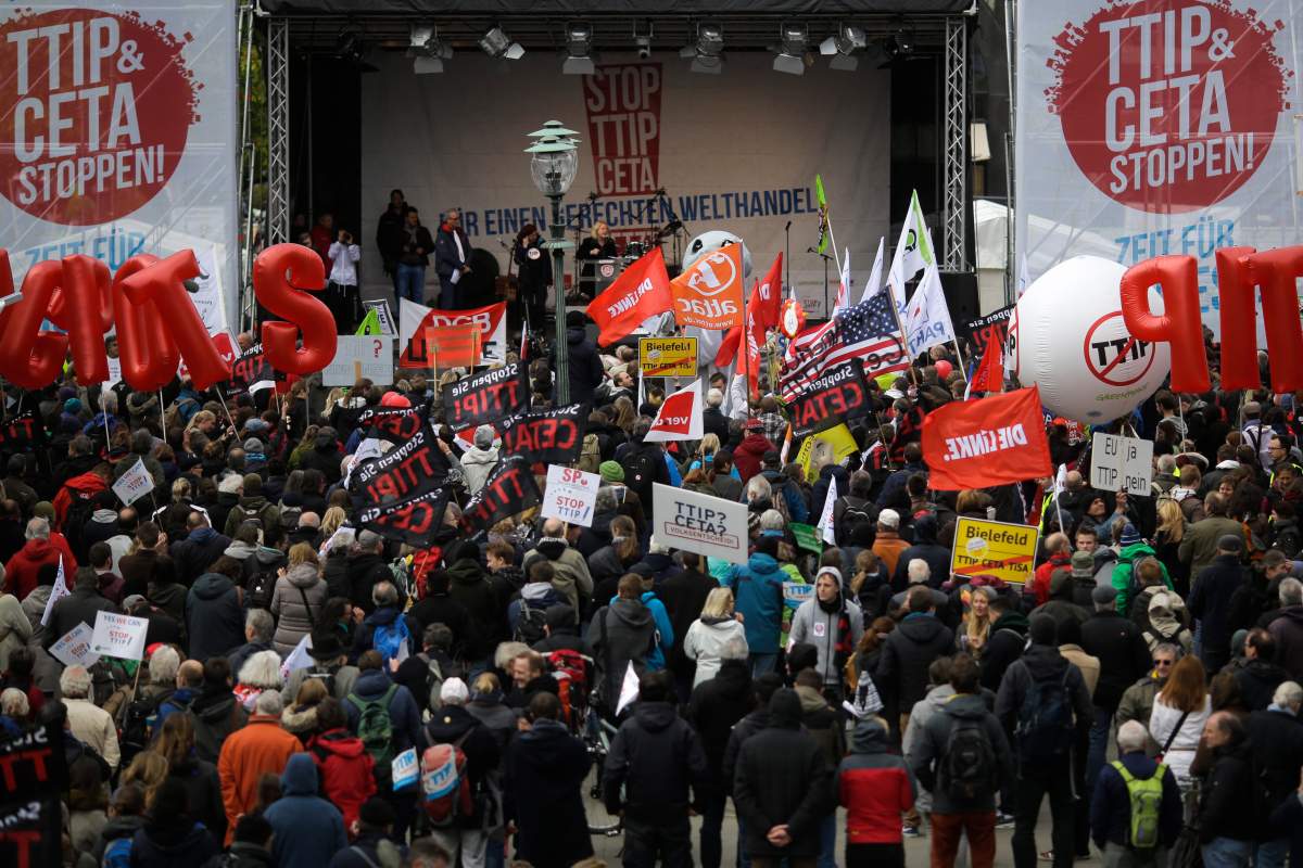 Protestors gather in front of the main stage during a demonstration of thousands of people against the planned Transatlantic Trade and Investment Partnership, TTIP, and the Comprehensive Economic and Trade Agreement, CETA, ahead of the visit of United States President Barack Obama in Hannover, Germany, Saturday, April 23, 2016. The main slogan in the center reads: ‘Stop TTIP CETA for fair global trade’