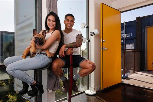 Patrick Tupas, right, with his wife, Maria Real-Tupas, who is holding their dog Moon Moon Fitzgerald, sit in the living room at their shipping container apartment in Phoenix. 