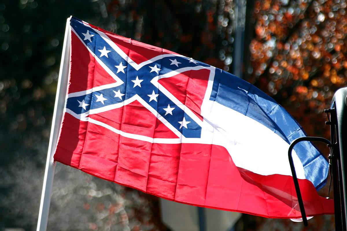 In this Tuesday, Jan. 19, 2016 photo, a state flag of Mississippi is unfurled by Sons of Confederate Veterans and other groups on the grounds of the state Capitol in Jackson, Miss., in support of keeping the Confederate battle emblem on the state flag.