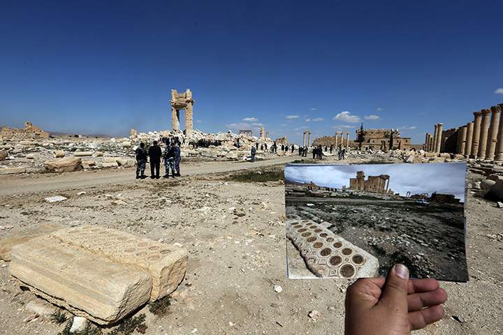 A general view taken on March 31, 2016 shows a photographer holding his picture of the Temple of Bel taken on March 14, 2014 in front of the remains of the historic temple in the ancient Syrian city of Palmyra.
