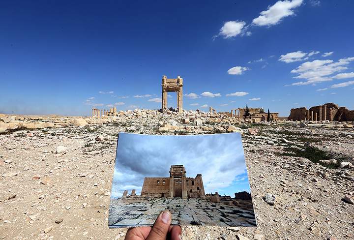 A general view taken on March 31, 2016 shows a photographer holding his picture of the Temple of Bel taken on March 14, 2014, in front of the remains of the historic temple in the ancient Syrian city of Palmyra.