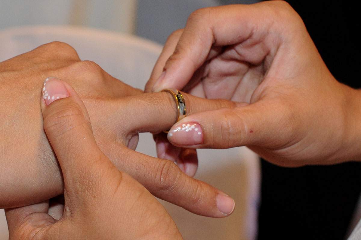A bride places a wedding band on the finger of her soon-to-be husband.
